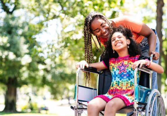 A little girl in a wheelchair enjoying a walk at the park with her mother.